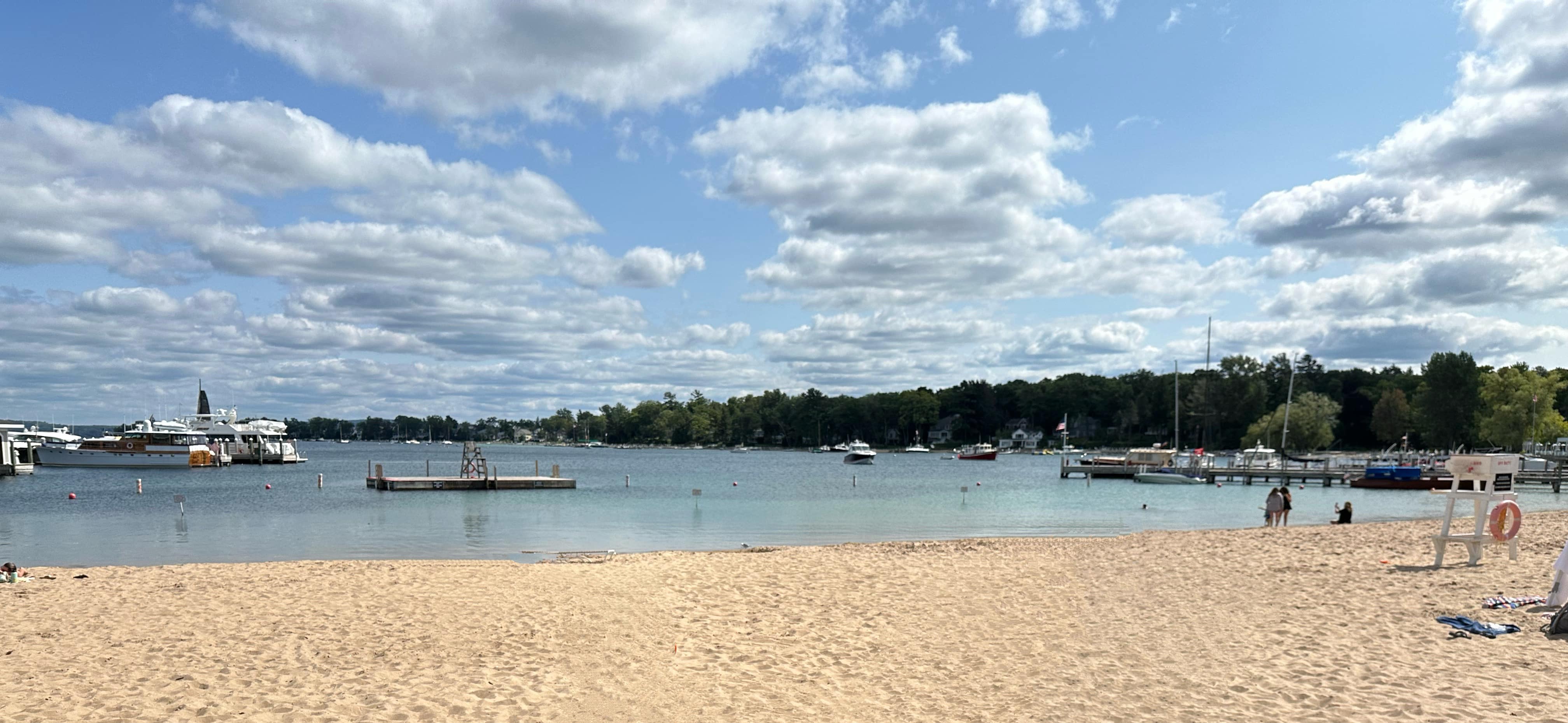 Zorn Park Beach in Harbor Springs Michigan with sandy shoreline, calm Little Traverse Bay water, marina docks, and boats under a blue sky