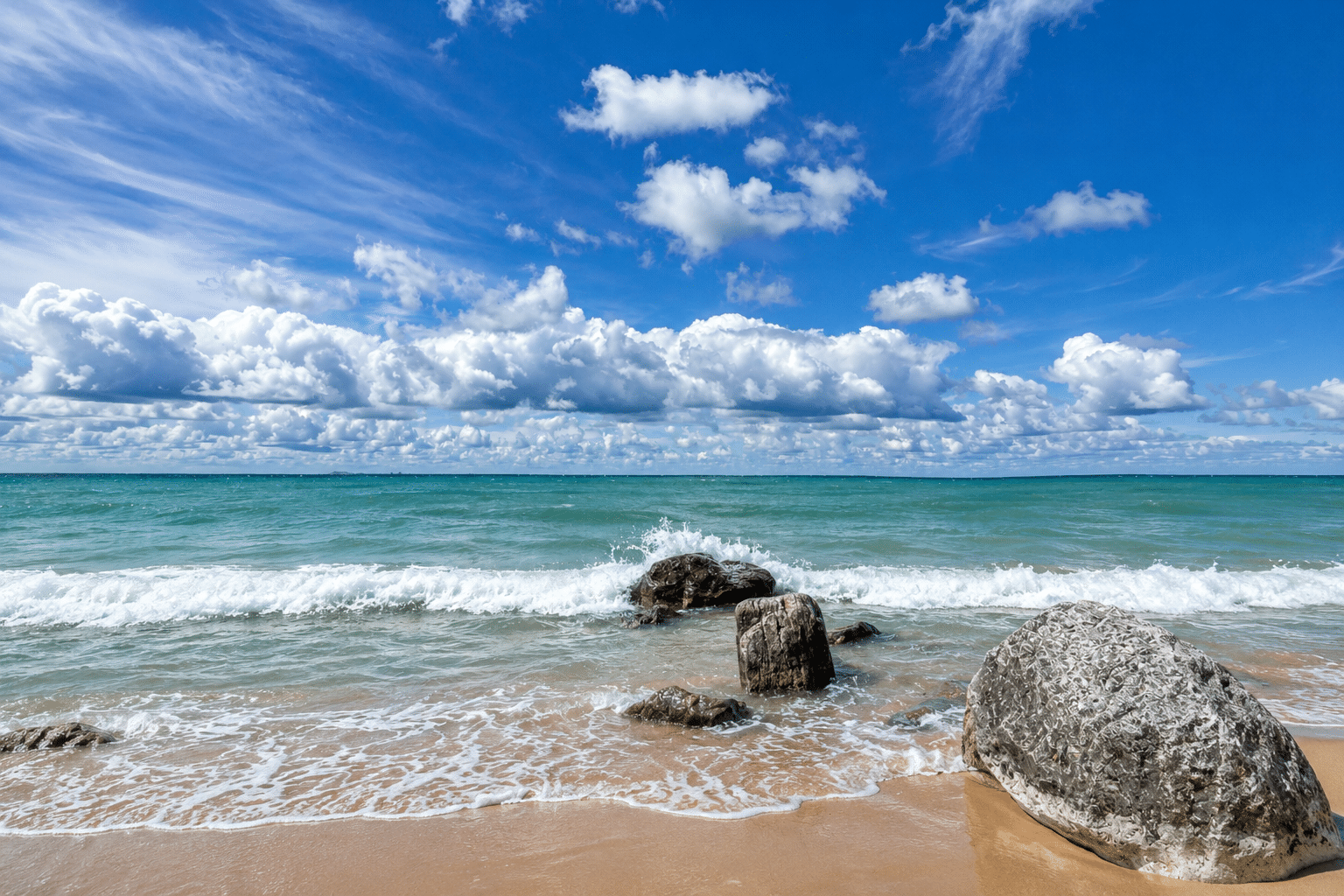Rocky Lake Michigan shoreline with turquoise water, rolling waves, and dramatic clouds near Harbor Springs on a bright summer day